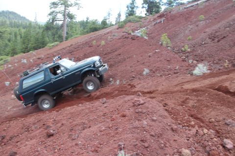 1995 Ford Bronco - A 1995 Ford Bronco navigates a challenging off-road terrain on a dusty, red slope.