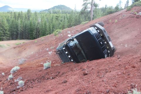 1995 Ford Bronco - A black SUV lies on its side after rolling down a steep, red dirt embankment.