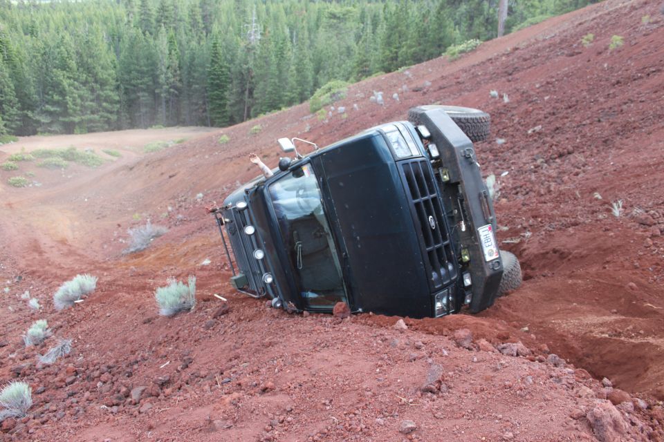 Black 1995 Ford Bronco rolled onto its side on a red dirt slope
