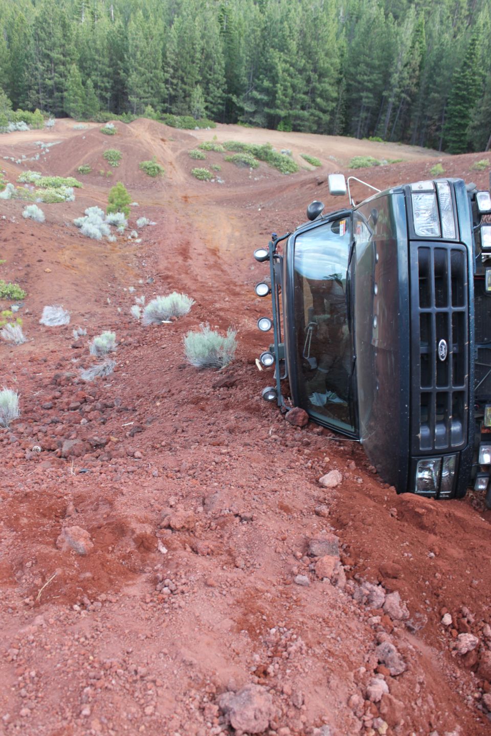 Truck tipped over on a dirt hill with trees in the background