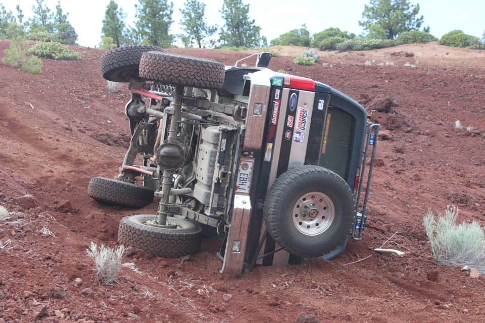 1995 Ford Bronco overturned on its side on a red dirt hill with sparse vegetation