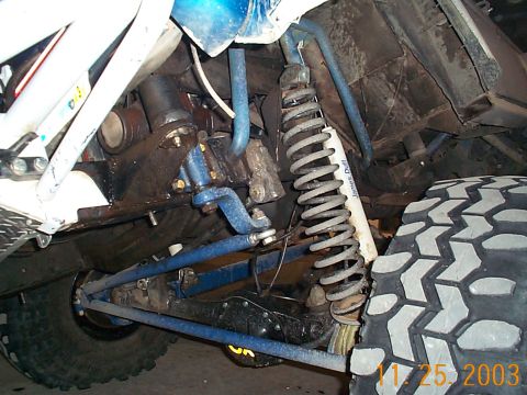 1977 Ford Bronco - Underbody shot of a lifted 4x4's front suspension showing blue-painted radius arms and a blue front axle housing, a coil spring over a whit…
