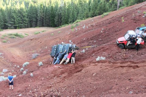 1995 Ford Bronco - A group of people attempts to free a stuck off-road vehicle on a steep, red dirt slope.