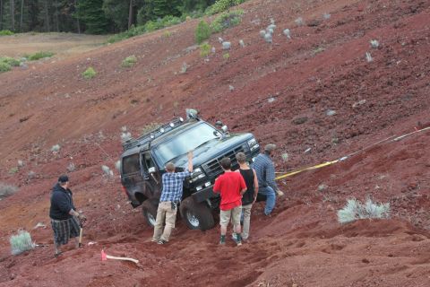 1995 Ford Bronco - A group of people attempt to free a black Ford Bronco from a steep, red dirt incline.