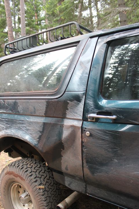 1995 Ford Bronco - This 1995 Ford Bronco shows extensive wear on its side paneling and door, with a roof rack visible.