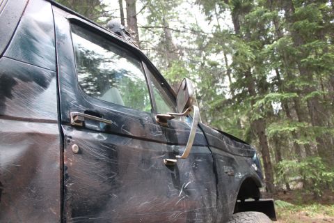 1995 Ford Bronco - A 1995 Ford Bronco sits in a forest, its dark green paint covered in numerous scratches from off-road use.