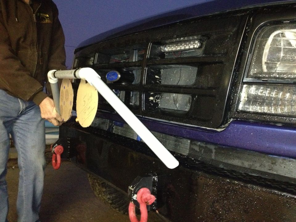 Front of a blue Ford Bronco with a black grille, aftermarket lights, and a PVC pipe rig holding two circular targets