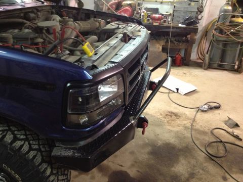 1996 Ford Bronco - Front view of a blue Ford truck's engine bay and custom bumper, parked indoors.