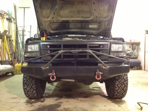 1996 Ford Bronco - This dark blue SUV is shown from the front with its hood open, revealing an aftermarket bumper and off-road tires.