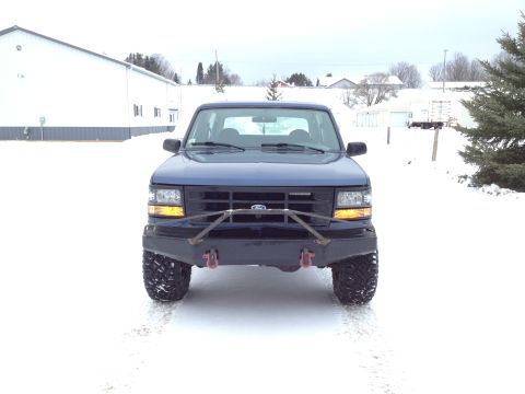 1996 Ford Bronco - A blue 1996 Ford Bronco is parked in the snow, an aftermarket bumper and large tires.
