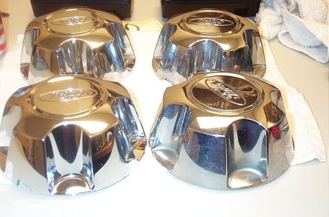 1991 Ford LTD Crown Victoria - Four chrome Ford hubcaps are displayed on a white cloth surface.