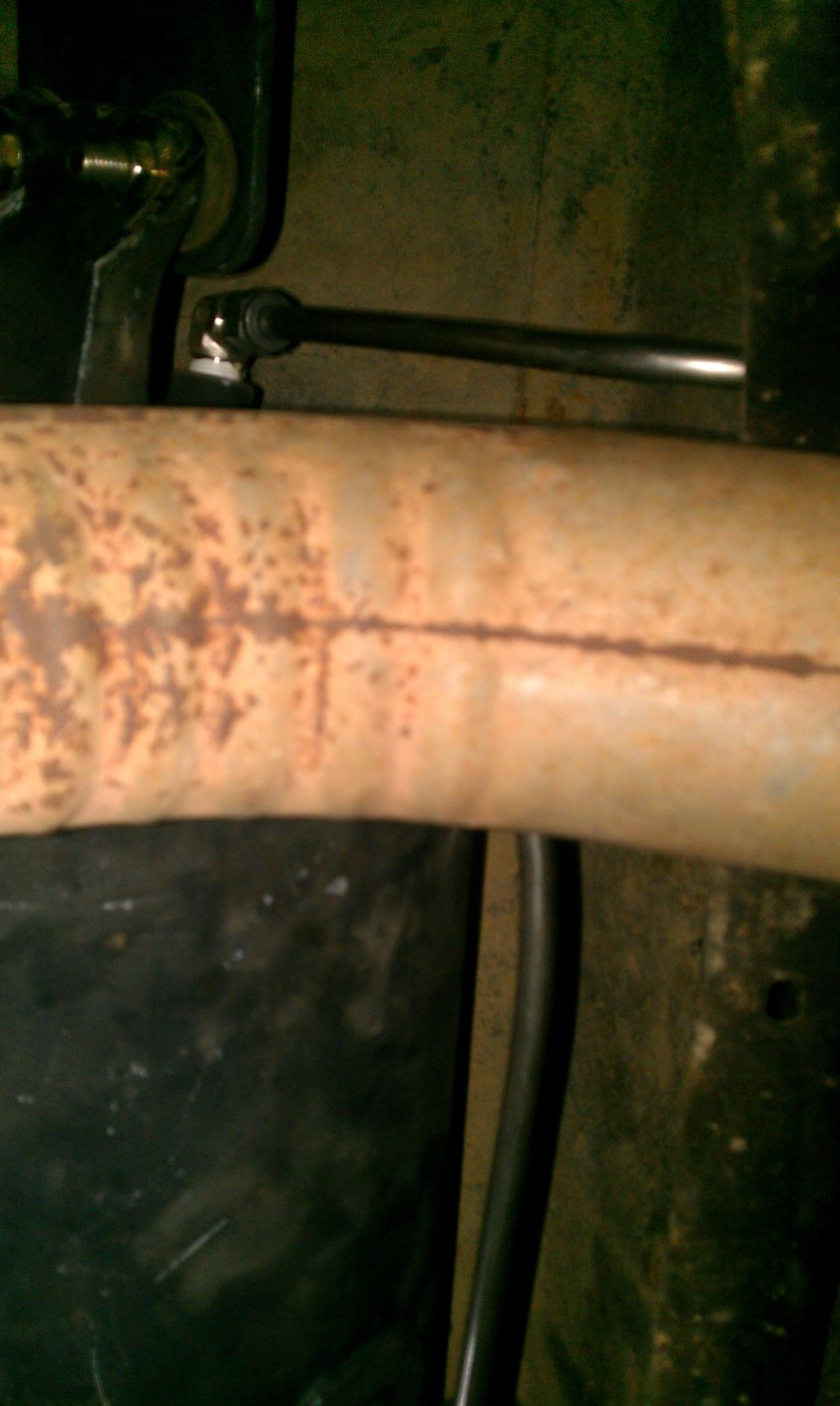 Close-up of a rusty exhaust pipe with a metal linkage rod attached to a bracket
