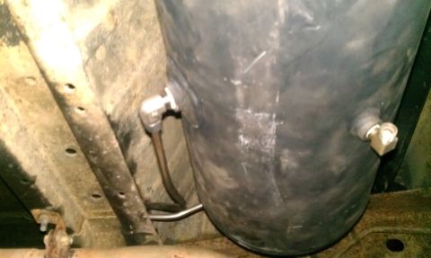 1995 Ford Bronco - Underside view of a black air tank with metal fittings mounted to a vehicle's chassis.
