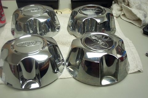 1991 Ford LTD Crown Victoria - Four Ford-branded chrome wheel center caps are displayed on a towel.