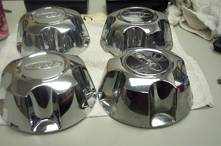 Four chrome wheel center caps with Ford logos are on a white towel