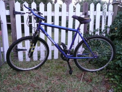 1994 Ford Bronco - A blue mountain bike is parked on grass in front of a white picket fence.