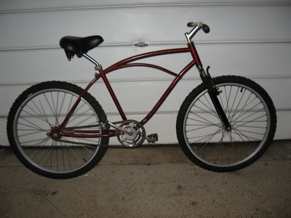 Red cruiser bicycle with black seat and tires, parked in front of a garage door