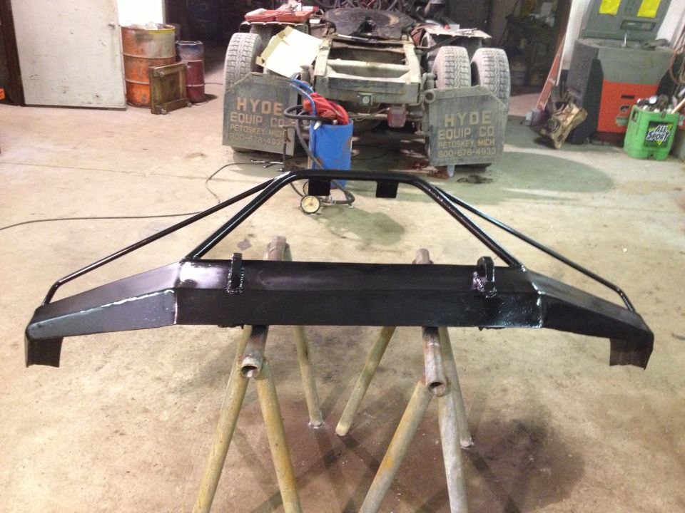Black custom front bumper on sawhorses in a workshop, with a truck chassis in the background