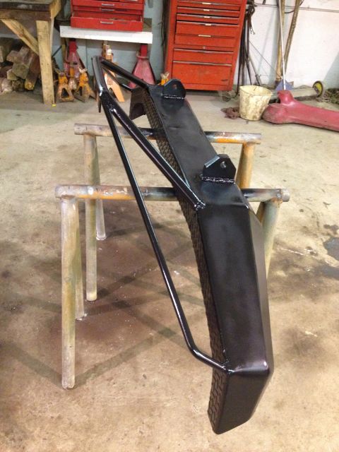1996 Ford Bronco - A freshly painted glossy black steel fabricated bracket or arm, likely a suspension radius arm or frame component, resting on tubular metal…