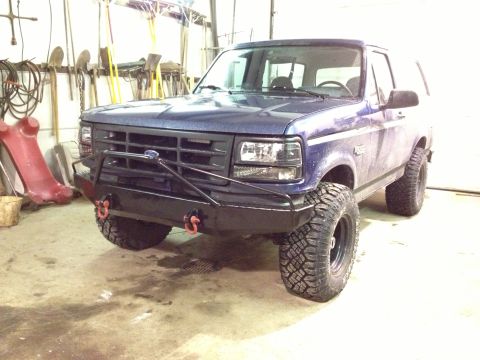 1996 Ford Bronco - A blue Ford Bronco with off-road tires and a custom bumper is shown from the front-three-quarter view in a garage.