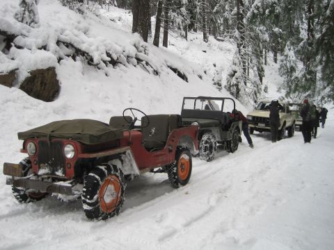 1989 Ford Bronco - Several vehicles navigate a snow-covered forest road, with some requiring snow chains.