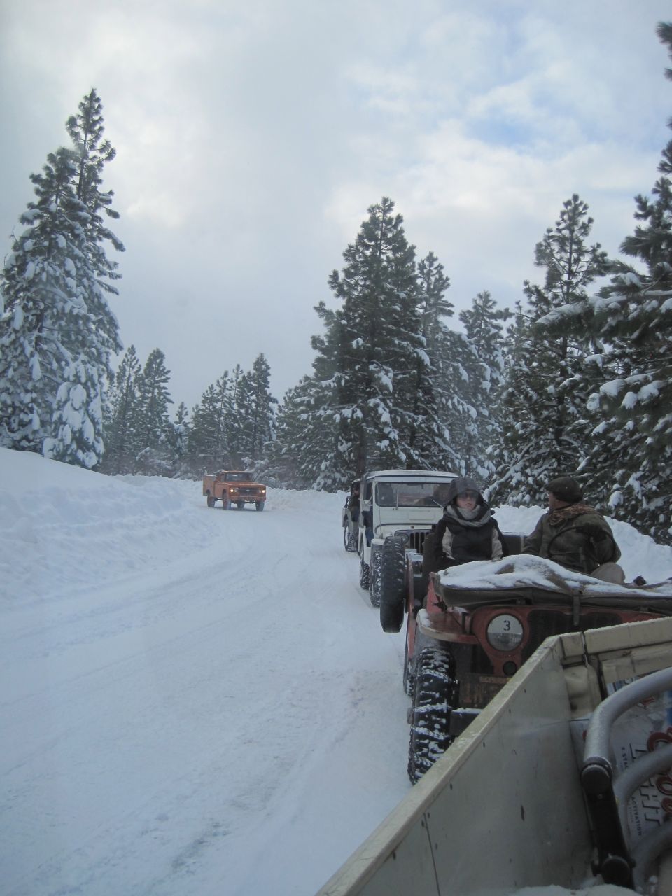 Several off-road vehicles driving on a snow-covered road through a forest