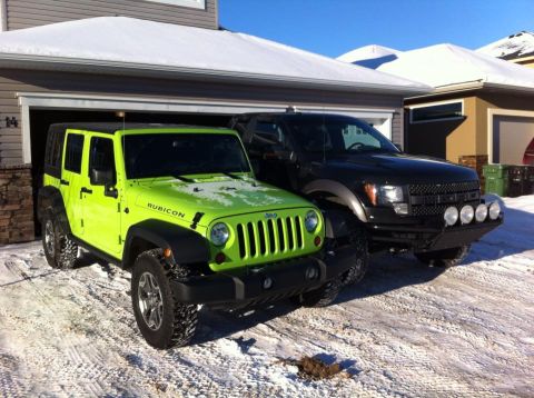 2013 Jeep Wrangler - Two trucks, a Jeep Wrangler and a Ford F-150 Raptor, sit in a driveway covered in snow.