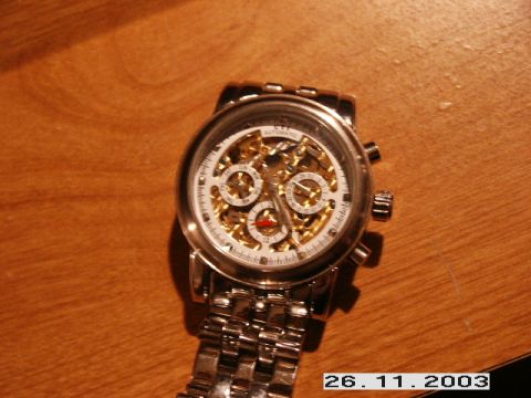 1998 Mercury Sable - A close-up of a silver automatic watch with a white face and visible internal gears, resting on a wooden table.