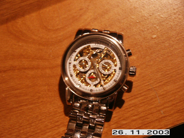 Silver metal watch with white face and exposed gears, on a wooden surface