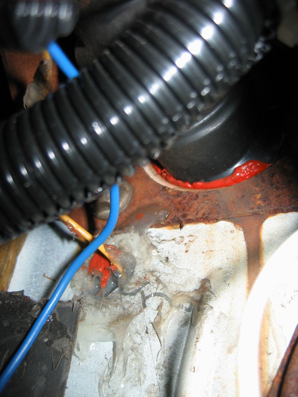 Close-up of automotive wiring harness and red sealant on rusty metal