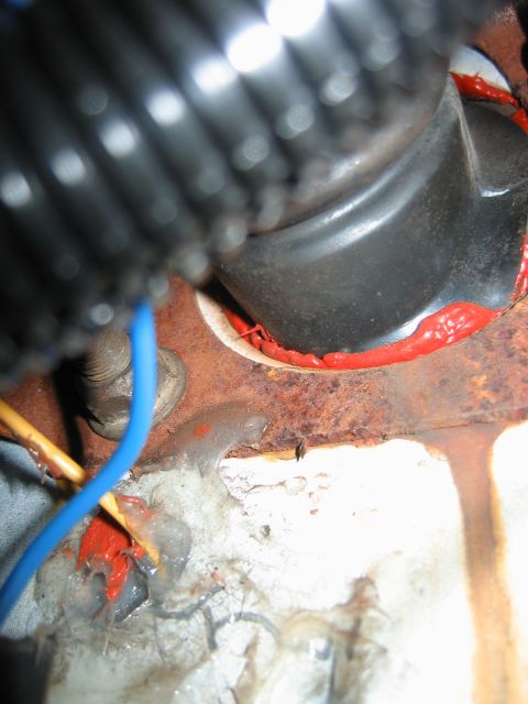 1992 Ford Bronco - This image shows a heavily rusted section of a vehicle's firewall with exposed wiring and red sealant applied around a grommet.