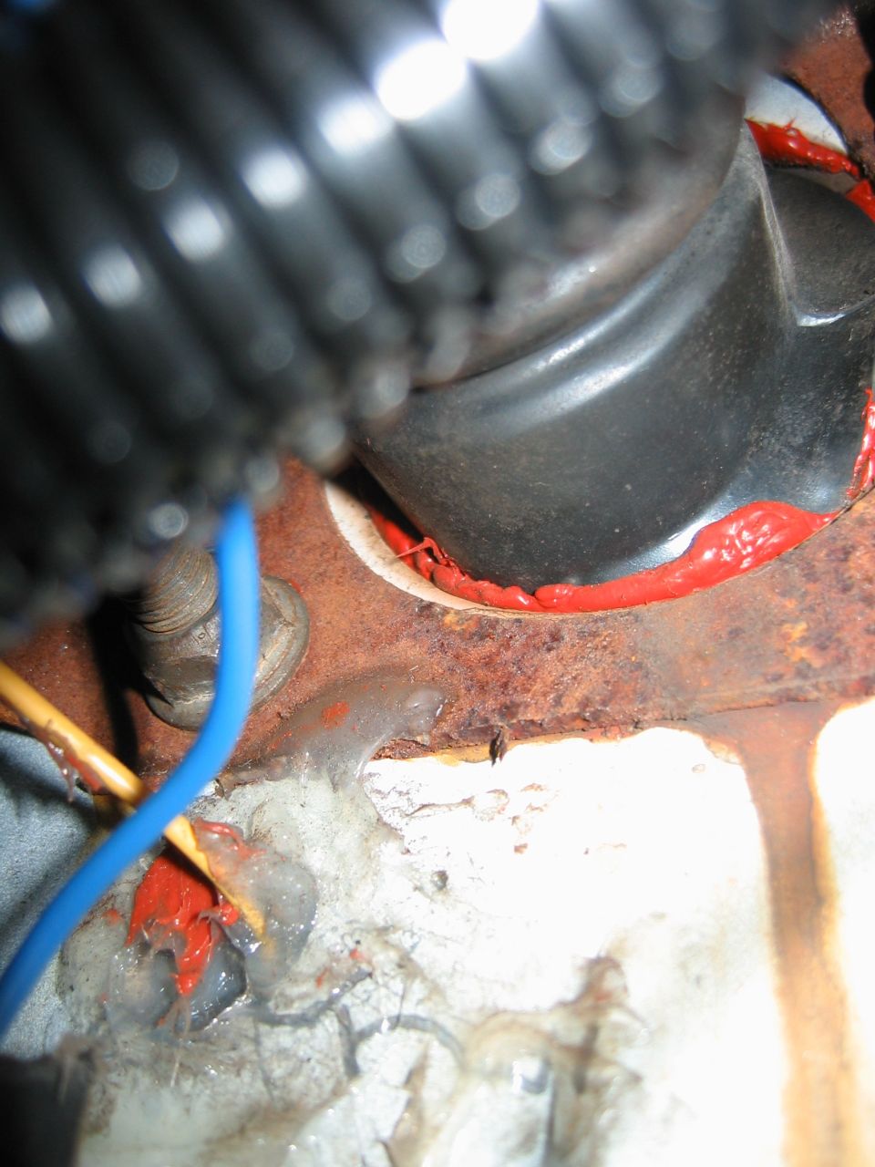 Close-up of rusted metal, wiring, and red sealant around a grommet on a vehicle's firewall