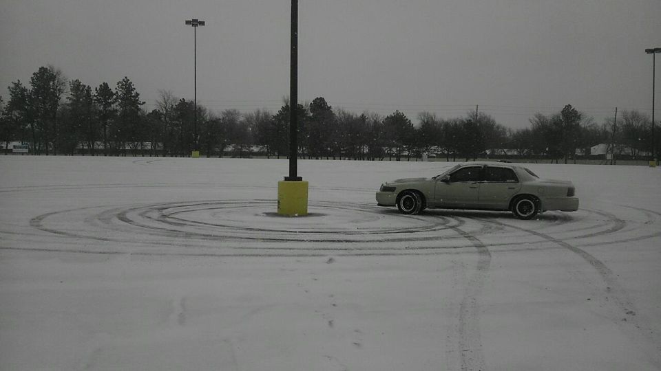 Silver sedan doing donuts in a snow-covered parking lot leaving tire tracks