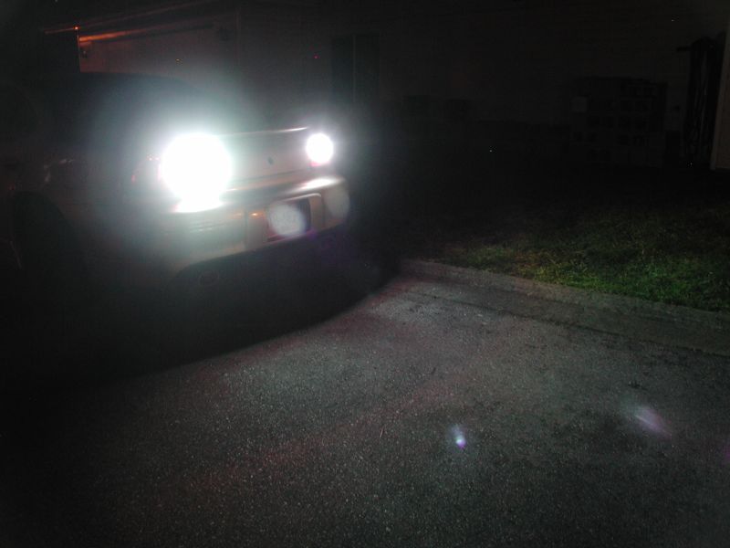 Car front with bright headlights on at night, asphalt and grass visible