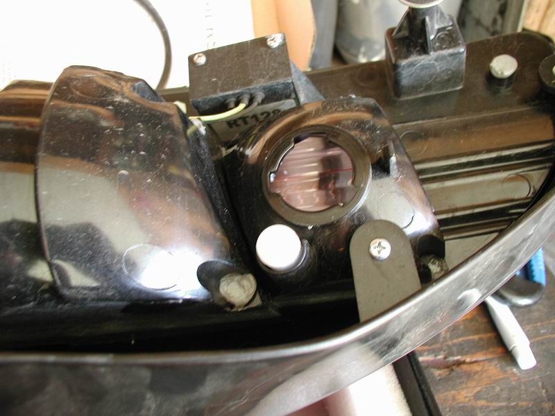 Close-up of a black car tail light assembly with a clear lens and internal components. A white circular bulb holder is visible