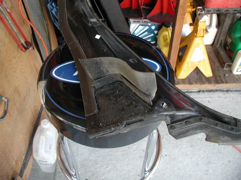 Black plastic car part with mesh and foam, resting on a black helmet with a blue Ford logo