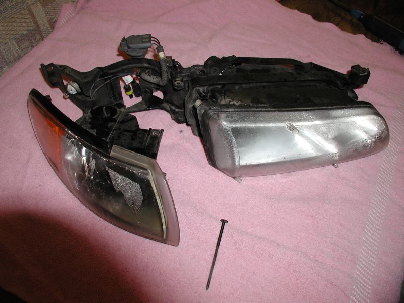 Car headlight assembly with orange turn signal lens and clear main lens, resting on a pink cloth. A nail is on the cloth next to it