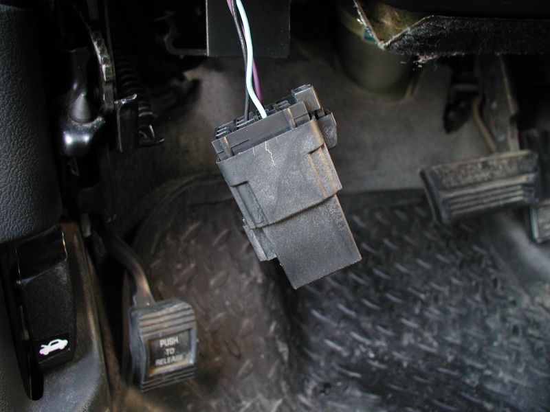 Wiring harness connector hanging near brake and gas pedals. Hood release lever visible