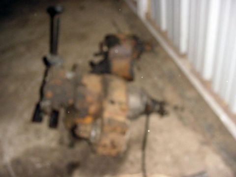 1992 Ford Bronco - Blurry shot of a rusty manual transmission and transfer case assembly sitting on a concrete garage floor next to a corrugated metal wall, w…