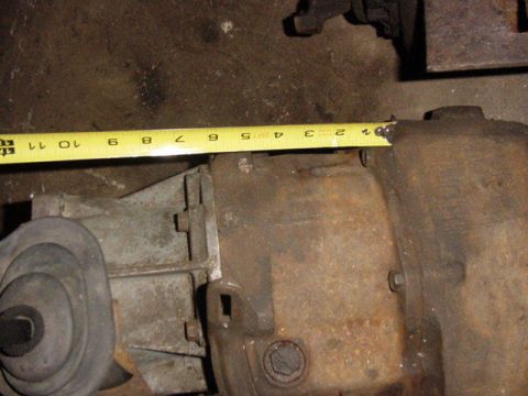 1992 Ford Bronco - A yellow tape measure stretched along the top of a rusty cast-iron transfer case or gearbox housing to check its length, roughly a foot of…