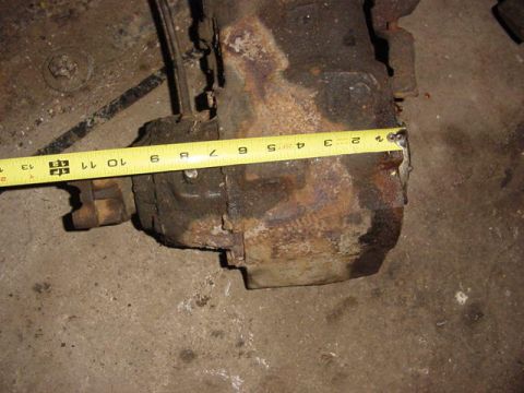 1992 Ford Bronco - A rusty cast-iron transfer case or gearbox housing sits on a concrete floor with a yellow tape measure stretched across it to document its…