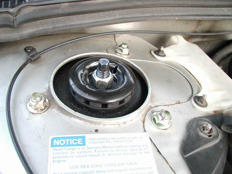 Close-up of a car's strut mount with a notice sticker about coolant