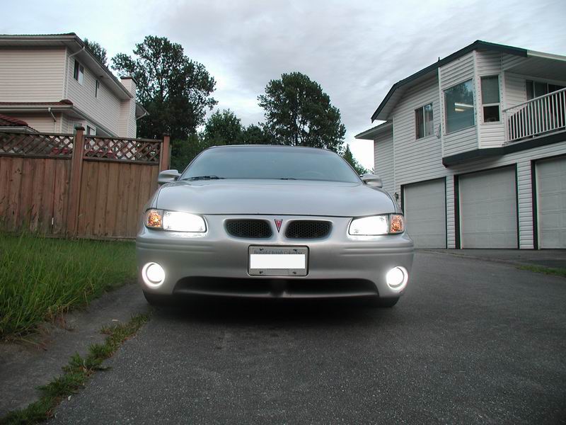 Silver 2002 Pontiac Grand Prix front view, headlights and fog lights on, parked in driveway