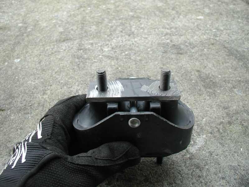 Black engine mount with two bolts, held in a gloved hand