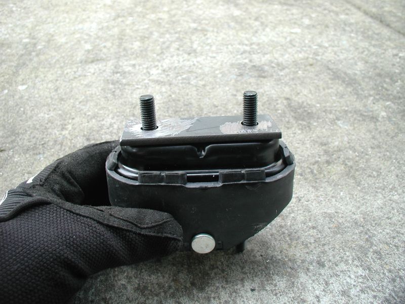 Gloved hand holding a black engine mount with two threaded studs