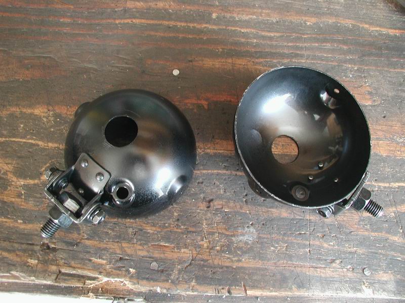 Two black headlight housings with mounting hardware, resting on a wooden surface