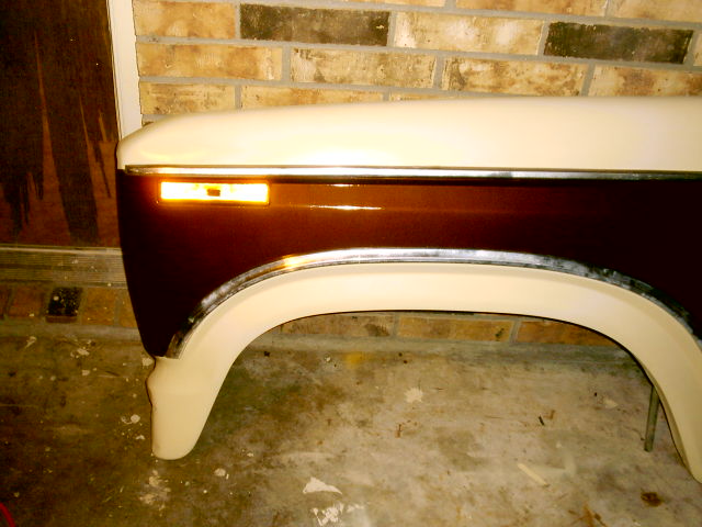 Cream and maroon truck fender with chrome trim and amber marker leaning against brick
