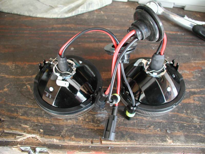 two black fog lights with red and black wires connected, sitting on a wooden surface
