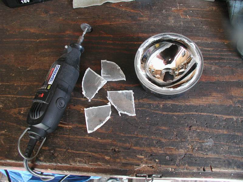 Broken fog light with Dremel tool and glass shards on wooden surface