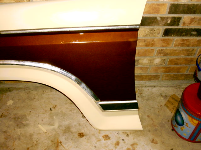Freshly painted brown and cream truck fender with chrome trim leaning on a brick wall